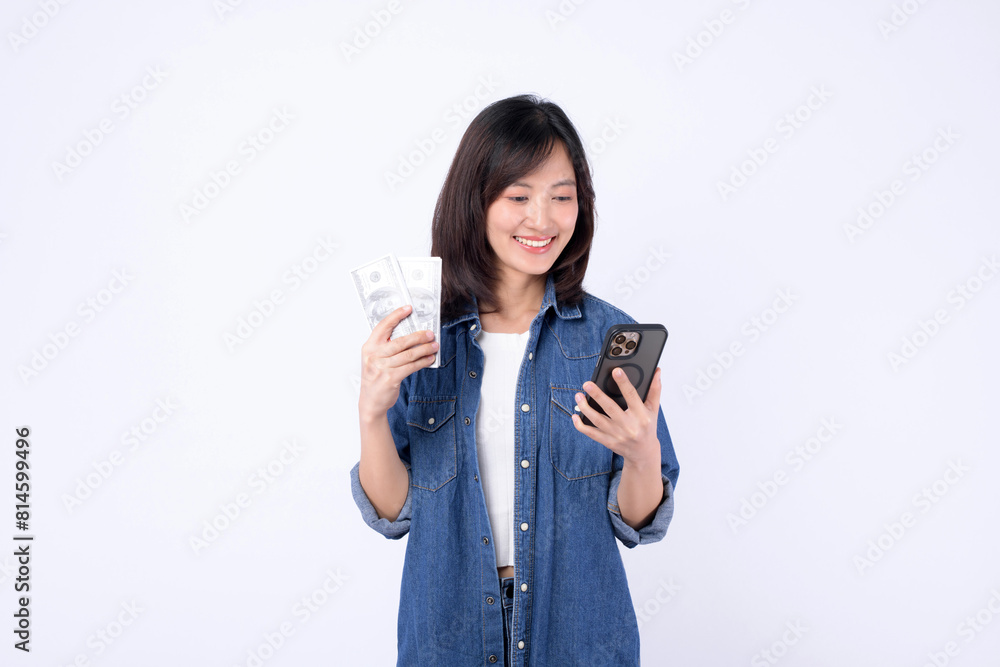 Asian woman wearing denim jean is holding dollar and a mobile phone against a white background, mobile banking concept. Asian woman wearing denim jean is holding dollar and a mobile phone against a white background, mobile banking concept.