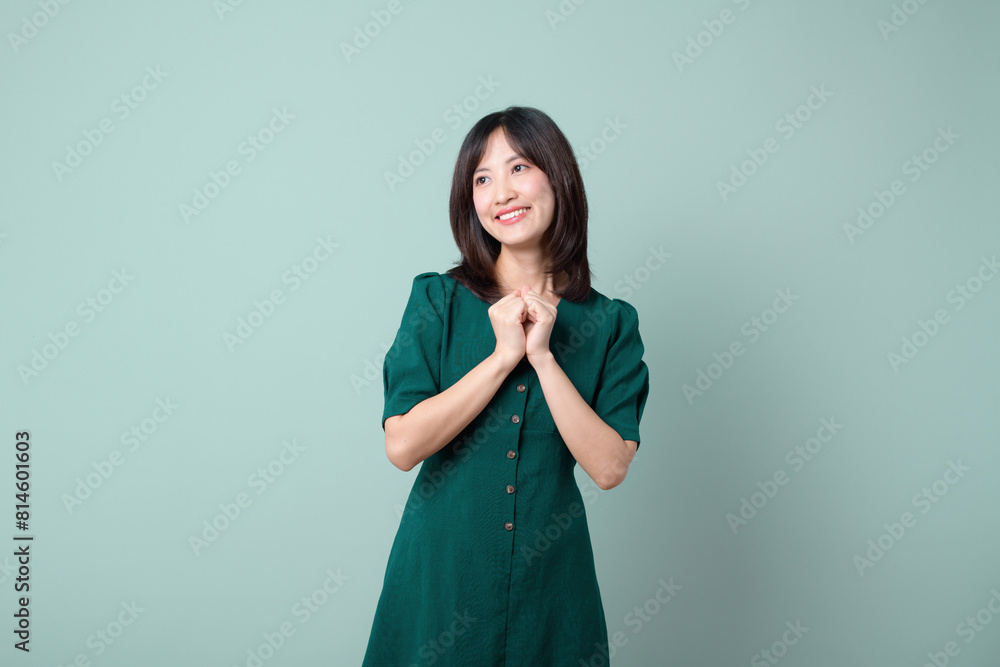 Adorable happy young asian woman model with shy emotion smiling expression cheerful positive attractive face and holding hand isolated on green pastel studio background. Portrait beautiful cute lady. Adorable happy young asian woman model with shy emotion smiling expression cheerful positive attractive face and holding hand isolated on green pastel studio background. Portrait beautiful cute lady.