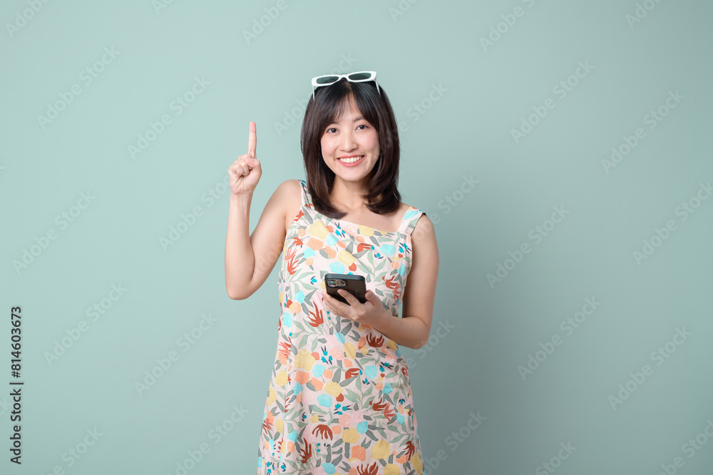 online payment, promotion, deals concept. Asian woman casual dress pointing finger to free copy space while using mobile phone isolated on pastel green background. online payment, promotion, deals concept. Asian woman casual dress pointing finger to free copy space while using mobile phone isolated on pastel green background.