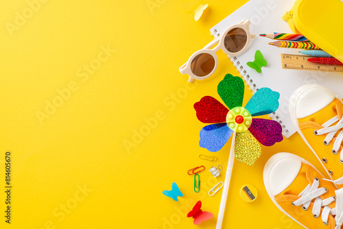 A playful and vibrant setup of summer school essentials including colorful sneakers, a pinwheel, stationery, and sunglasses on a bright yellow background