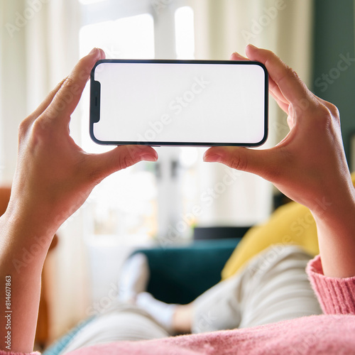 Close Up Of Woman Looking At Blank Screen Of Mobile Phone Lying On Sofa At Home Held Horizontally