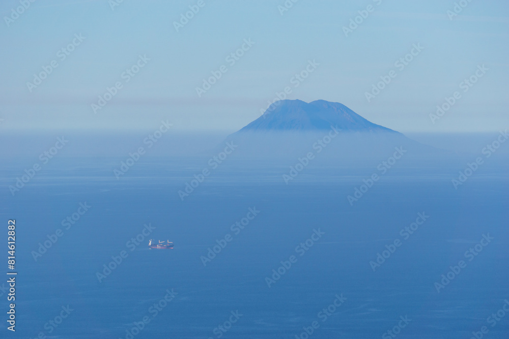 Distant Stromboli volcano with blue sea and sky on a hazy sunny day seen from Palmi, Calabria, Italy Distant Stromboli volcano with blue sea and sky on a hazy sunny day seen from Palmi, Calabria, Italy