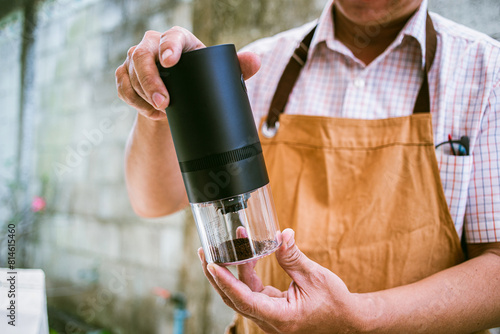 barista presenting a portable coffee grinder in a close-up shot, highlighting essential brewing equipment and coffee beans © Akira Kaelyn