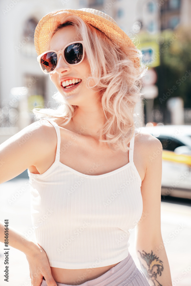 Young beautiful smiling blond hipster woman in trendy summer clothes. Carefree female posing in the street at sunny day. Positive model outdoors at sunset. Cheerful and happy in hat, sunglasses Young beautiful smiling blond hipster woman in trendy summer clothes. Carefree female posing in the street at sunny day. Positive model outdoors at sunset. Cheerful and happy in hat, sunglasses