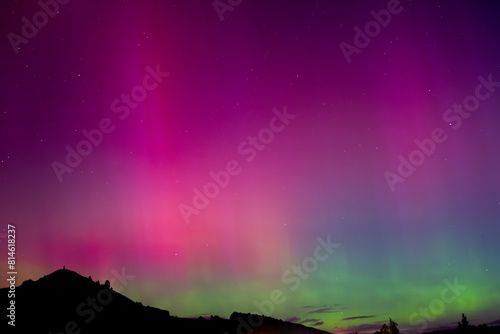 Pink and green Aurora Australis over Puketapu mountain in Palmerston, Otago. Palmerston is located in the South Island of New Zealand, where the southern lights can be seen. 