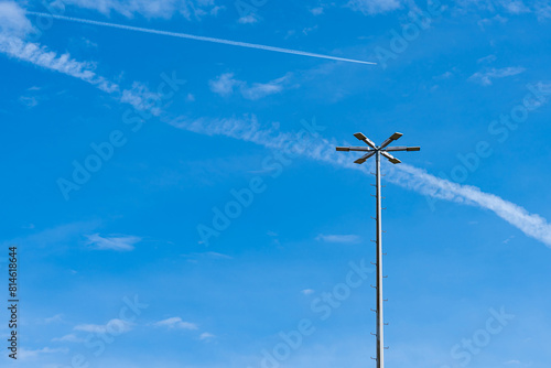 Tapeta Vertical metal mast with lighting lanterns against a background of blue sky with light clouds
