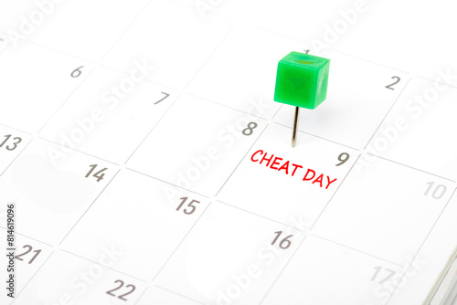 Cheat day written on  a calendar with a green push pin to remind you and important appointment.