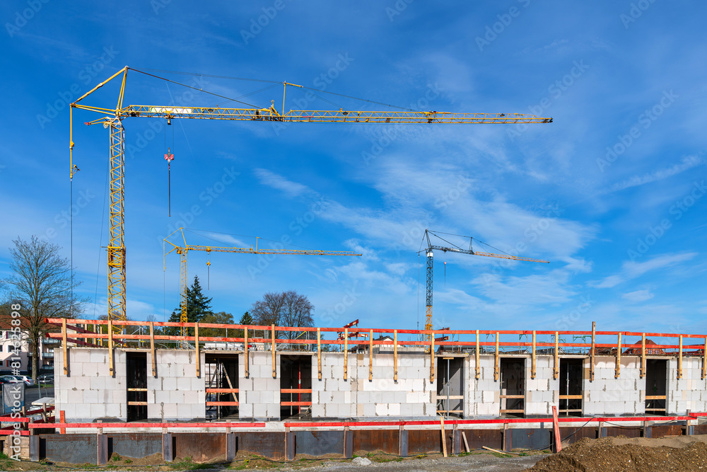 Part of a building under construction with the first floor erected and tower cranes against the background of a blue sky with light clouds. Part of a building under construction with the first floor erected and tower cranes against the background of a blue sky with light clouds.