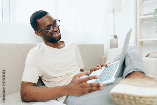 Smiling African American Man Typing on Laptop while Working from Home on a Modern Sofa