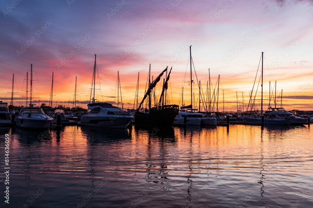 many sail boats in the water with a sun set behind them many sail boats in the water with a sun set behind them