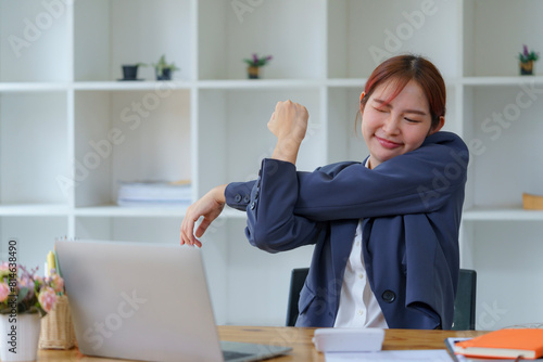Asian businesswomen feel tired from hard work, thus doing arm stretching to relax the body. Tired Asia woman stretching her hands while working in an office.