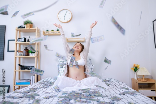 happily pregnant woman sitting on bed in her bedroom and enjoying  a lot of money full room. Monetary expenses for pregnancy and childbirth.