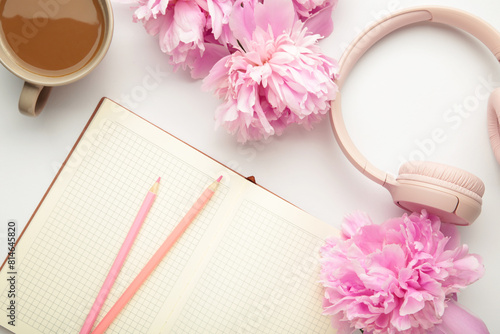 Modern pink headphones with flowers peonies and notebook on light background