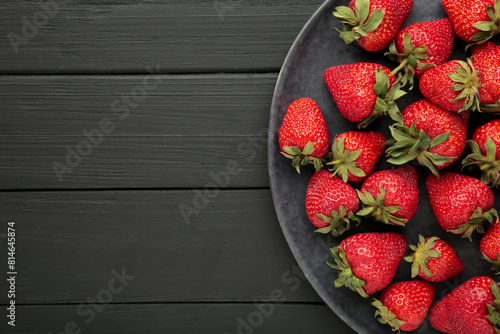 Top of view fresh strawberry in dark plate on black wooden background.