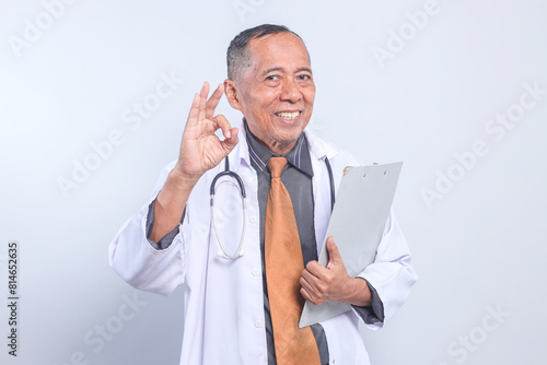 Professional Senior Doctor Holding Paperlist And Showing Ok Sign Isolated On White Background photo