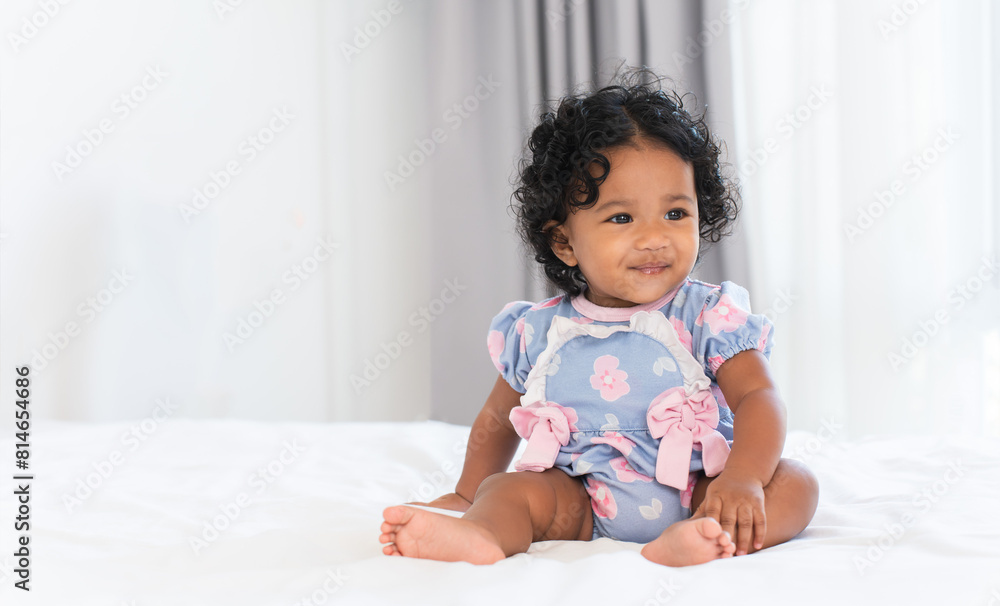 Cute African little newborn 7 months old baby girl wearing clothes with black curly hair sitting on white bed in bedroom at home. Happy adorable small daughter smiling. Copy space Cute African little newborn 7 months old baby girl wearing clothes with black curly hair sitting on white bed in bedroom at home. Happy adorable small daughter smiling. Copy space