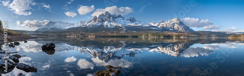 A tranquil lake mirroring the grandeur of snow-capped mountains under the gentle light of dawn, as the sky, awash with soft hues of blue and clouds, completes this picturesque landscape. A scattering 