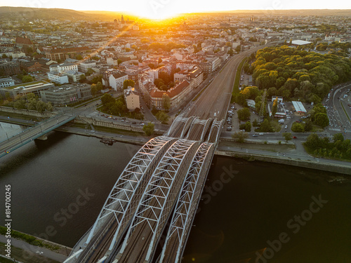 Panorama of Krakow with a railway bridge in the foreground and Wawel Castle in the background at sunset, captured by a drone.