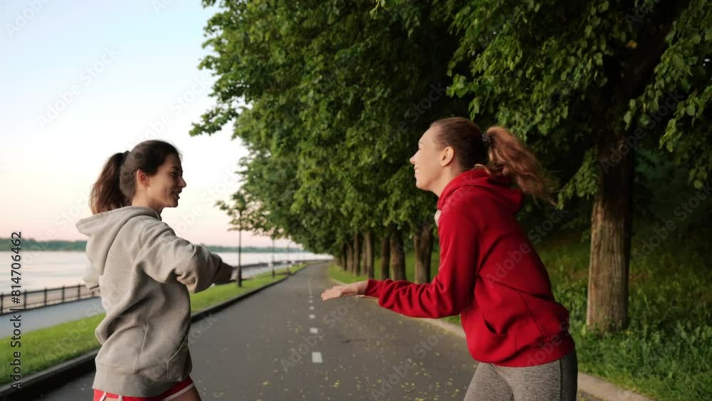 Warm up before training. Two happy young girls are talking to each other and doing muscle stretching. Playing sports with friends in the fresh air. Concept of workout, healthy lifestyle, fitness. Warm up before training. Two happy young girls are talking to each other and doing muscle stretching. Playing sports with friends in the fresh air. Concept of workout, healthy lifestyle, fitness.