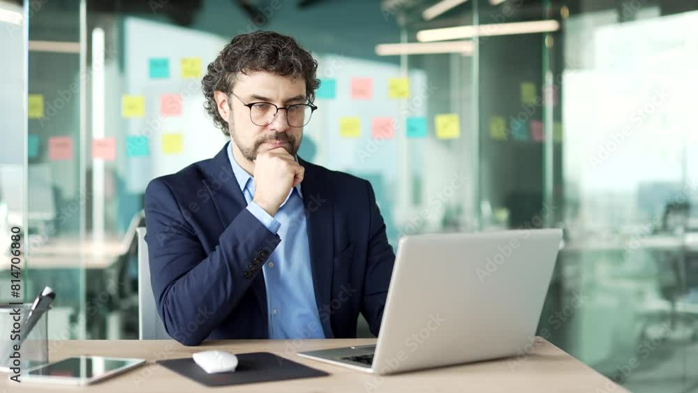 Serious thoughtful businessman in a formal suit works on a laptop sitting at a workplace in a business office. Entrepreneur is thinking about solving a problem, busy with a startup project on computer Serious thoughtful businessman in a formal suit works on a laptop sitting at a workplace in a business office. Entrepreneur is thinking about solving a problem, busy with a startup project on computer