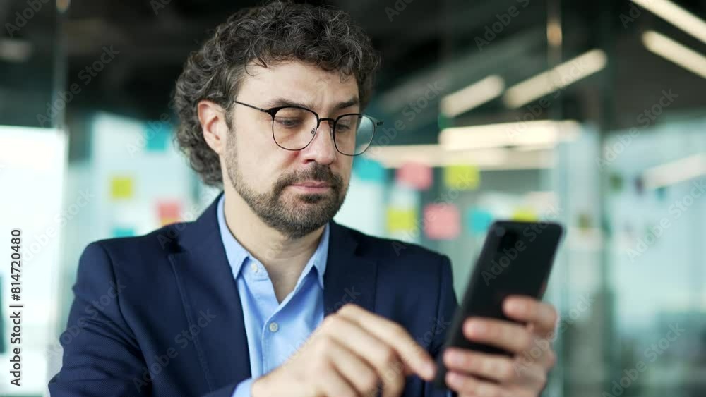 Thoughtful businessman is using phone sitting at workplace in business office. Man worker works on a mobile application, typing a message, chatting with a client or browsing the web online. Close up Thoughtful businessman is using phone sitting at workplace in business office. Man worker works on a mobile application, typing a message, chatting with a client or browsing the web online. Close up