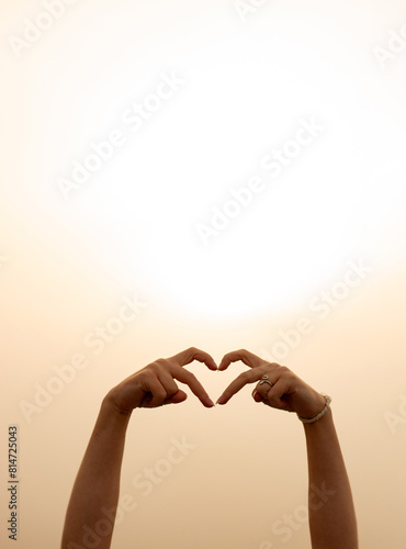 hands of a girl making a heart on the background of sunrise or sunset