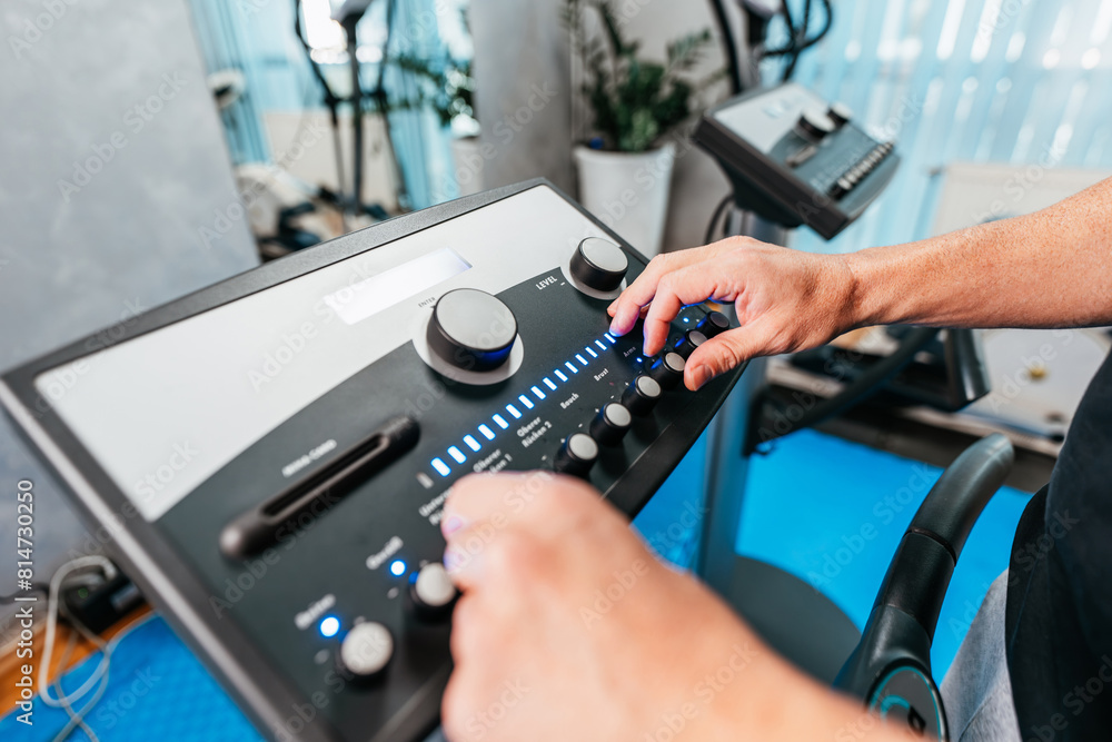 Professional physiotherapist working with beautiful young woman in EMS suit during special electro stimulation training or treatment. Close up shot on therapist's hands on EMS machine control panel.