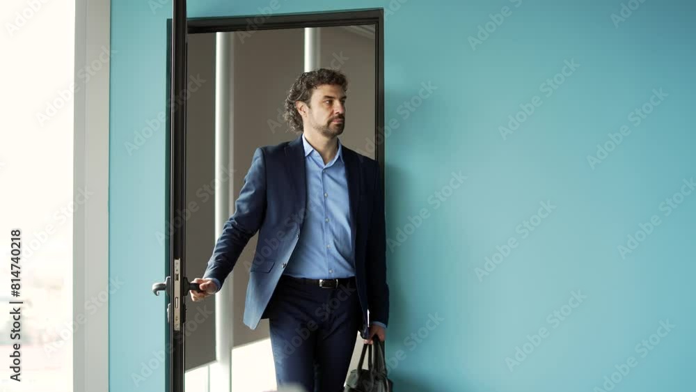 A bearded businessman in a formal suit opens a door in a modern building and walks out of office into the hall or corridor. Man worker or entrepreneur and with briefcase in his hands leaves workplace A bearded businessman in a formal suit opens a door in a modern building and walks out of office into the hall or corridor. Man worker or entrepreneur and with briefcase in his hands leaves workplace