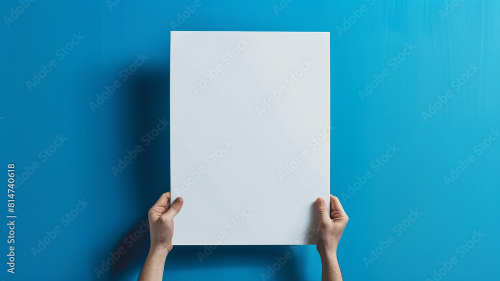 hand holding white blank poster template on blue background hand holding white blank poster template on blue background