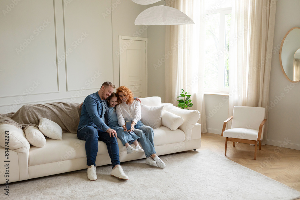 Cheerful parents and kid daughter making selfie on cellphone, having fun and resting on couch at home in large living room, free space Cheerful parents and kid daughter making selfie on cellphone, having fun and resting on couch at home in large living room, free space