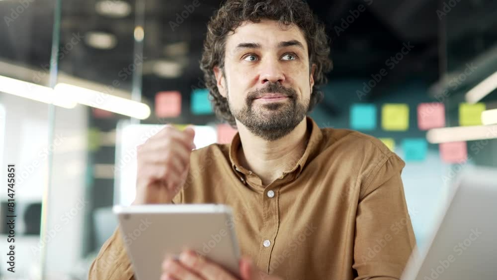 Thoughtful businessman is using digital tablet sitting at workplace in business office. Man worker works on application, typing a message, chatting with a client or browsing the web online. Close up