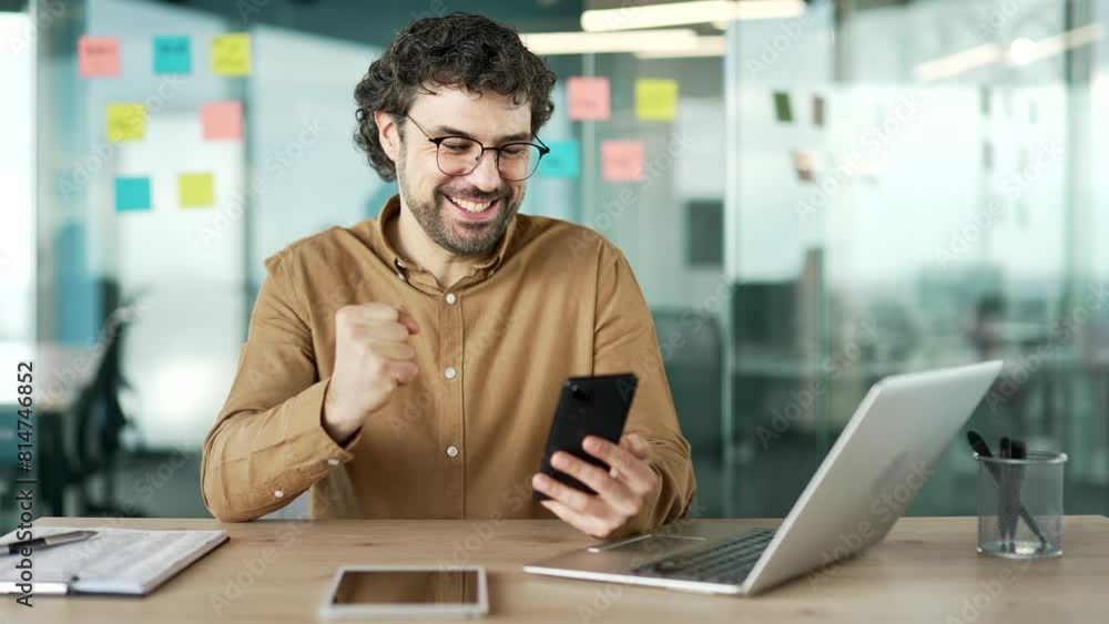 Satisfied happy businessman received great news on mobile phone while sitting at workplace in business office. Smiling glad bearded mature man worker reads a positive good message on the smartphone Satisfied happy businessman received great news on mobile phone while sitting at workplace in business office. Smiling glad bearded mature man worker reads a positive good message on the smartphone