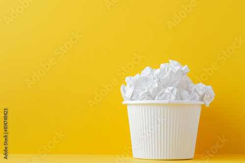 White Wastebasket Overflowing with Crumpled Paper on Yellow Background photo