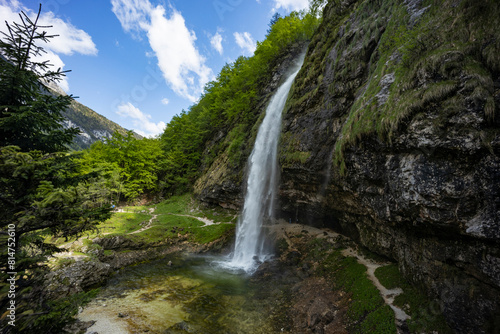 Fototapeta Naklejka Na Ścianę i Meble -  Fontanon of Goriuda, Udine. Wonderful waterfall that falls from a cliff. The force of the waterfall is a sight to behold. Hiking, trekking in the open area surrounded by woods. Summer holidays, peace.