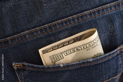 A close-up shot of a one hundred dollar banknote in the back pocket of blue jeans