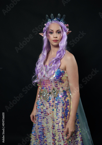 artistic portrait of beautiful female model with long purple hair and elf ears, wearing a fantasy fairy crown, wearing a rainbow glitter sequin ball gown. Standing in side profile, isolated on dark st photo