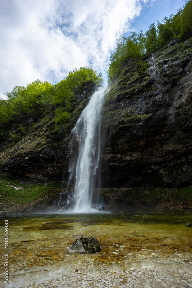 Fototapeta premium Fontanon of Goriuda, Udine. Wonderful waterfall that falls from a cliff. The force of the waterfall is a sight to behold. Hiking, trekking in the open area surrounded by woods. Summer holidays, peace.