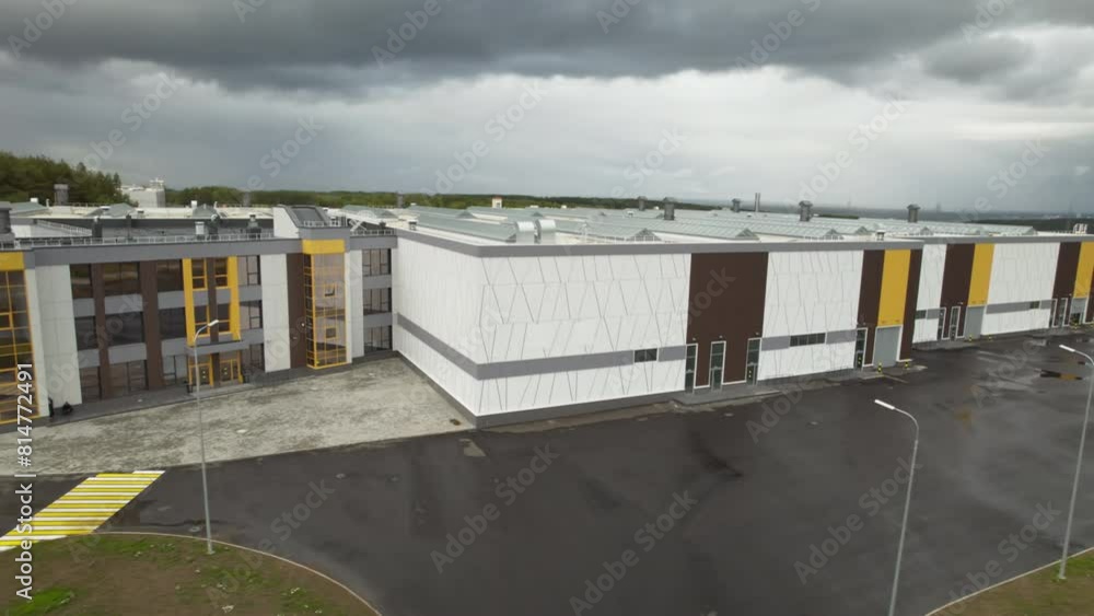 Distribution center building with glass facade under grey cloudy sky. Manufacturing plant warehouse at countryside area aerial view Distribution center building with glass facade under grey cloudy sky. Manufacturing plant warehouse at countryside area aerial view