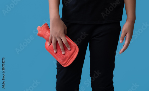 Woman using hot water bottle to leg pain on light blue background