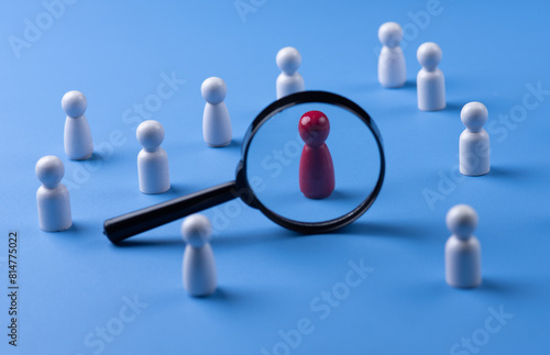 A magnifying glass and a red wooden figures with blur business man who search for someone who ‘s special person. Concept of Human resources management and recruitment.