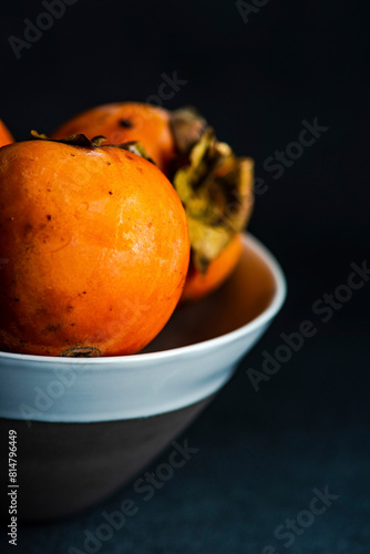 Ripe persimmon fruits in the bowl on stone background photo