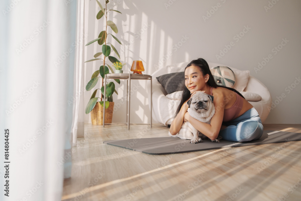Affectionate young asian woman embracing her pug dog on yoga mat, sharing a tender moment in sunny room Affectionate young asian woman embracing her pug dog on yoga mat, sharing a tender moment in sunny room