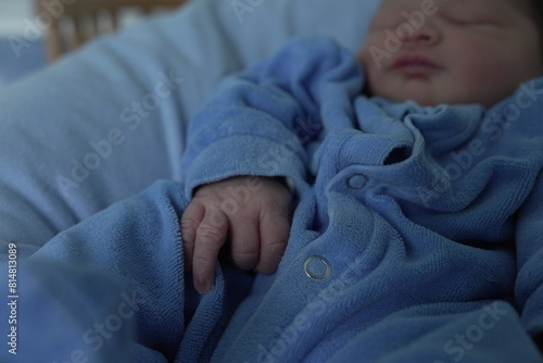 A close-up of a newborn baby’s hand resting on a blue onesie. The tiny fingers and delicate skin are highlighted, capturing the tender and fragile nature of a newborn. © Marco