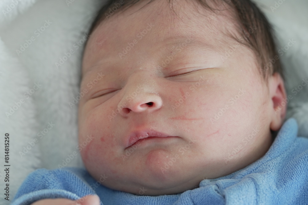 A close-up of a newborn baby’s face, eyes closed in peaceful slumber, capturing the essence of innocence and serenity in a blue onesie. A close-up of a newborn baby’s face, eyes closed in peaceful slumber, capturing the essence of innocence and serenity in a blue onesie.