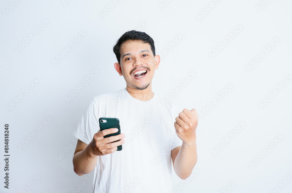 Adult Asian man showing happy gesture while looking to his mobile phone Adult Asian man showing happy gesture while looking to his mobile phone