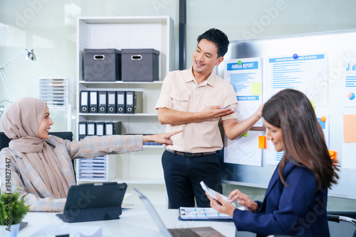 Comprehensive financial chart adorns the whiteboard during a presentation  where male and female business professionals  including a Muslim woman in hijab  engage in a productive meeting.