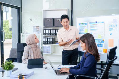 Tableau sur toile Comprehensive financial chart adorns the whiteboard during a presentation, where male and female business professionals, including a Muslim woman in hijab, engage in a productive meeting