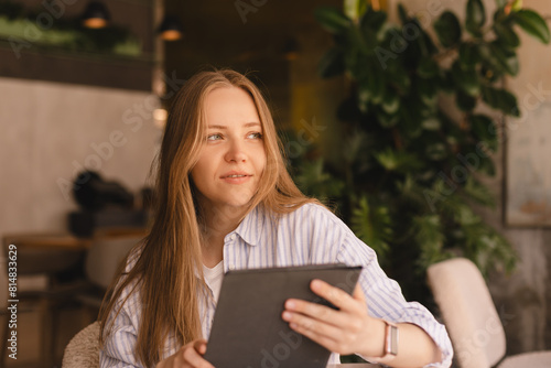 Attractive happy smiling blonde woman wear shirt sitting with tablet computer in cafe. Beauty girl student using tablet computer for social media, studying or reading news. Female look at side.