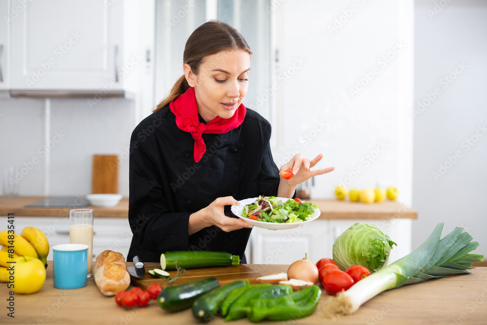 Smiling female chef in black uniform preparing vegetable salad in private kitchen Smiling female chef in black uniform preparing vegetable salad in private kitchen