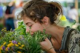 A young woman is smelling a bunch of fresh herbs. She has her eyes closed and looks relaxed. The photo is taken from the side and her hair is in a ponytail.